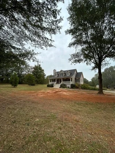 Cleared residential lot with mulch, mature trees removed, colonial home visible in background